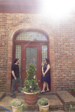 Couple standing by a red arched door on a sunny brick building.