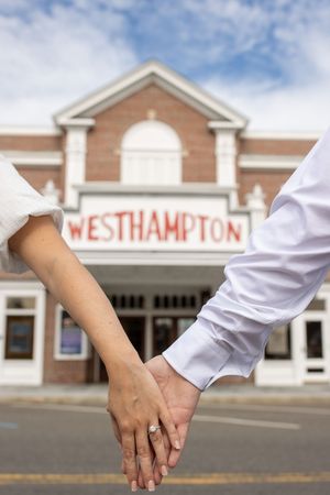 Engaged couple holding hands in front of the historic Westhampton theater building.