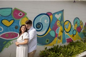 Couple sharing a tender embrace against a vibrant colorful heart-themed graffiti mural wall.