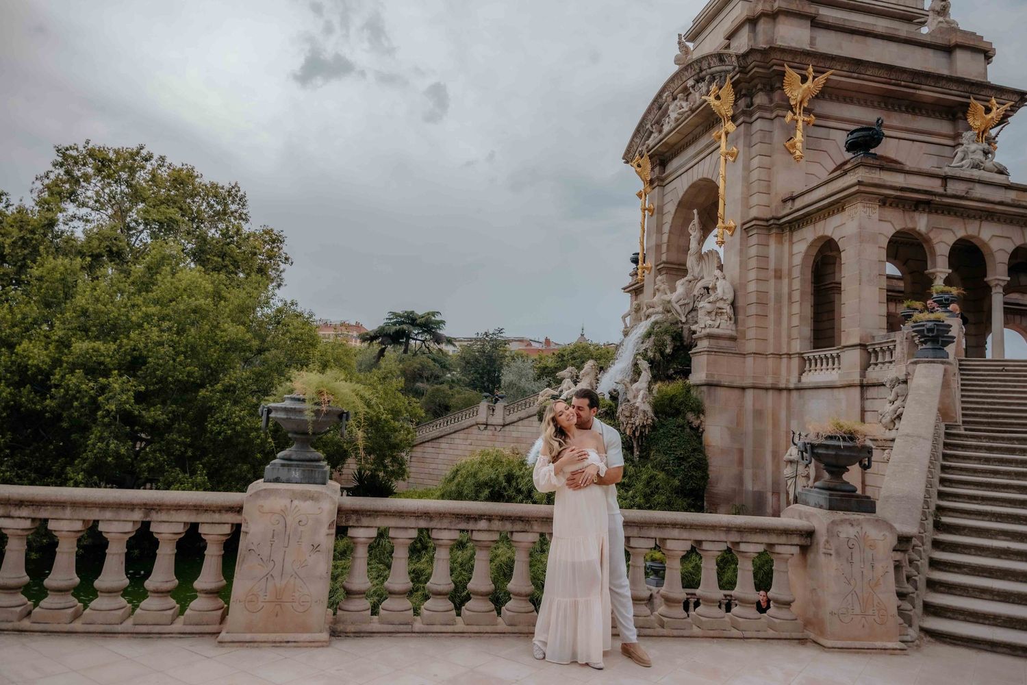 A radiant expectant mother standing on the sweeping stone staircase of the Cascada Monumental fountain in Ciutadella Park.