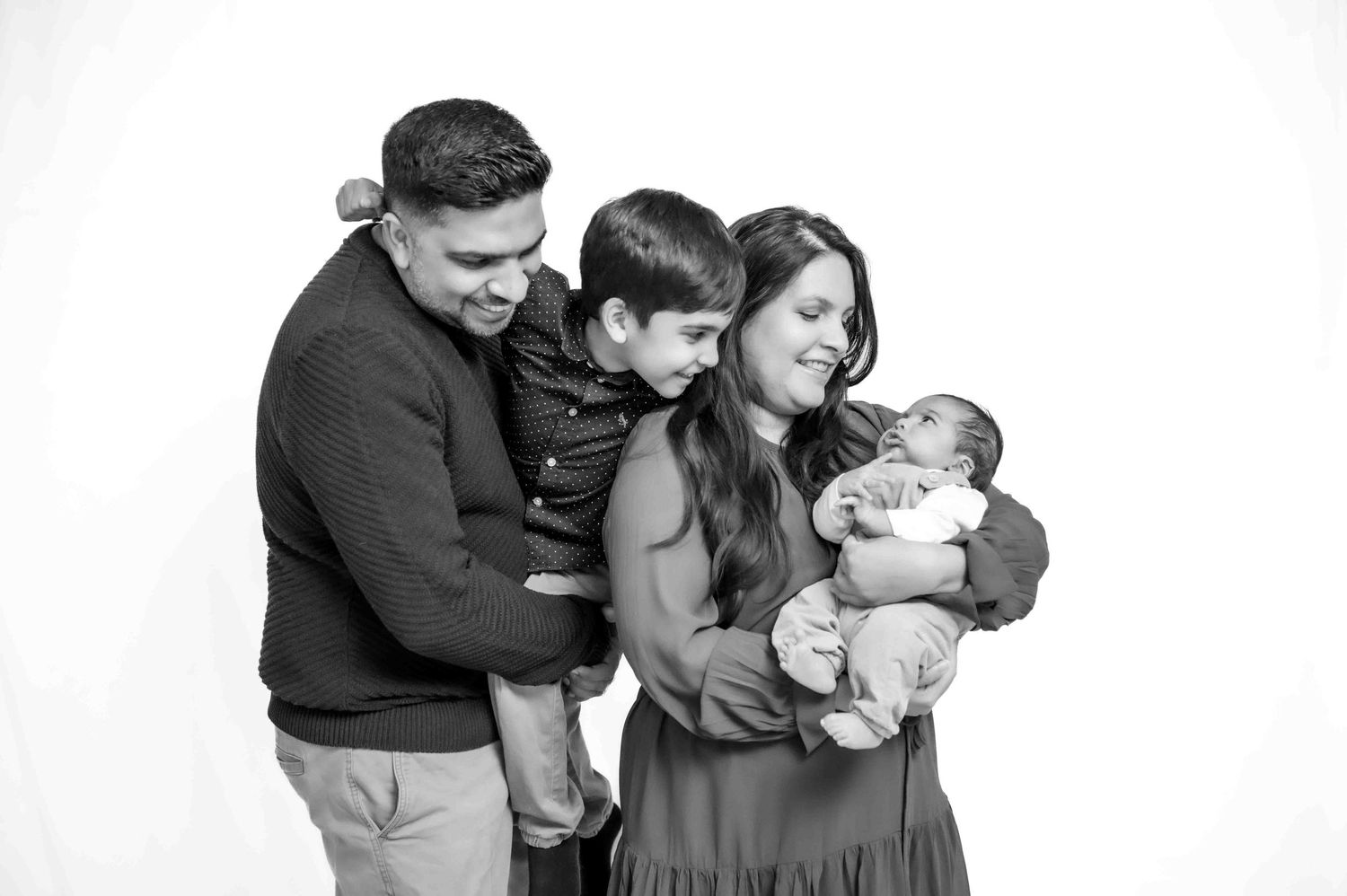 Black and white family portrait with parents holding two young children, smiling against a white background.