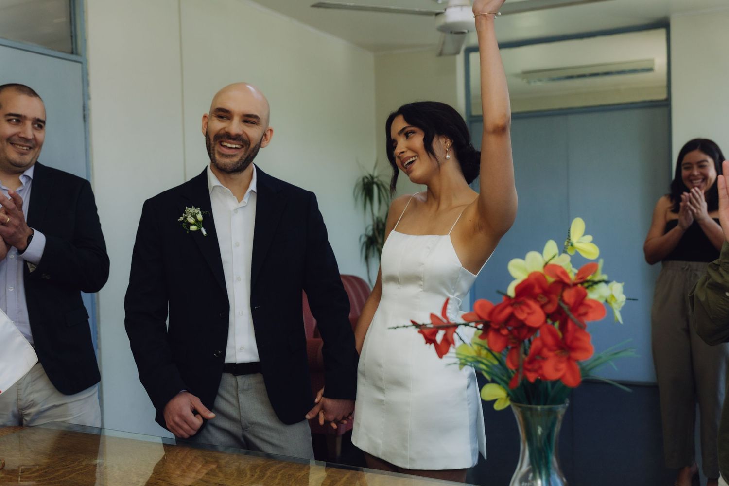 Joyful bride raises arm in celebration beside smiling groom holding hands after civil wedding ceremony.
