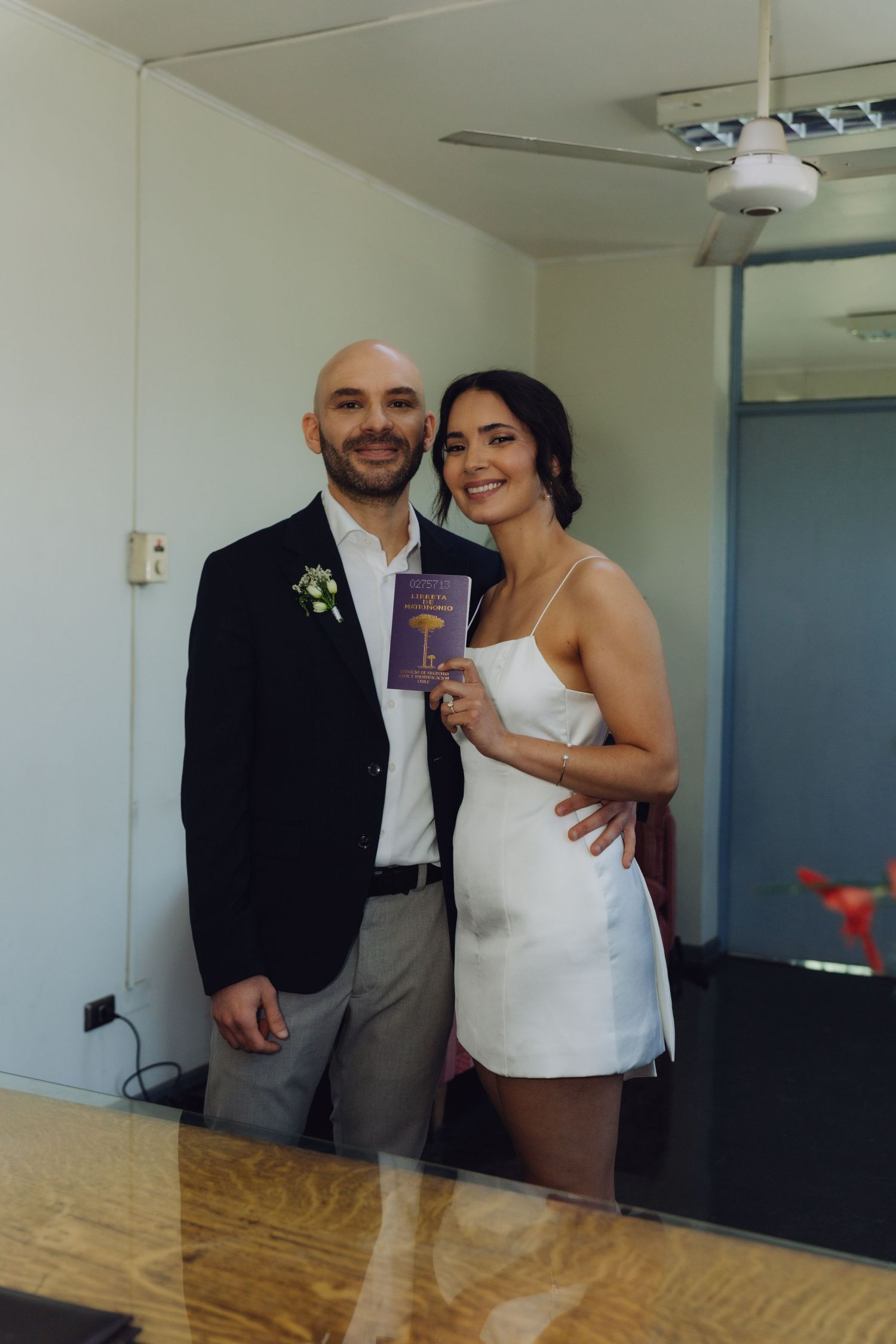 Happy newlyweds smile together as bride proudly displays purple marriage certificate after ceremony.