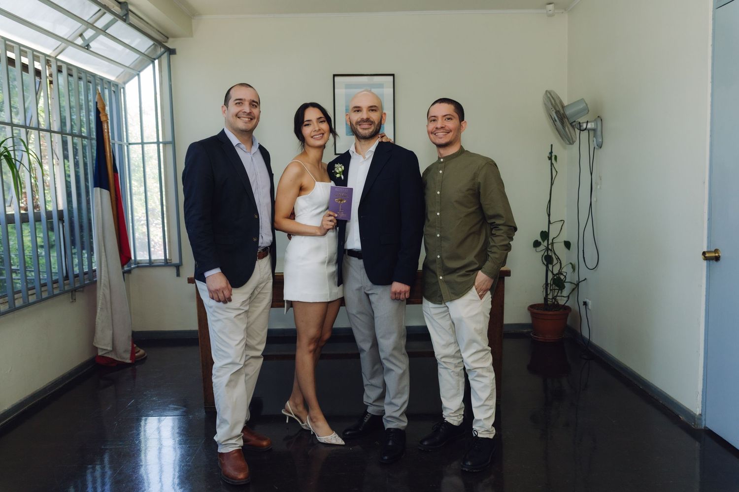 Group of four people including bride in white dress and groom smiling at civil wedding ceremony.