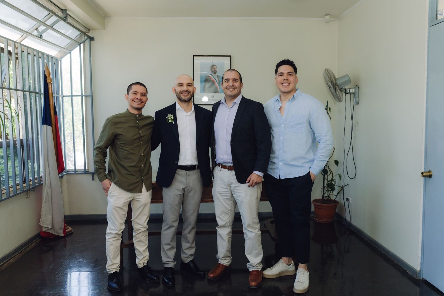 Four men in smart casual attire posing together indoors with a flag in the background.