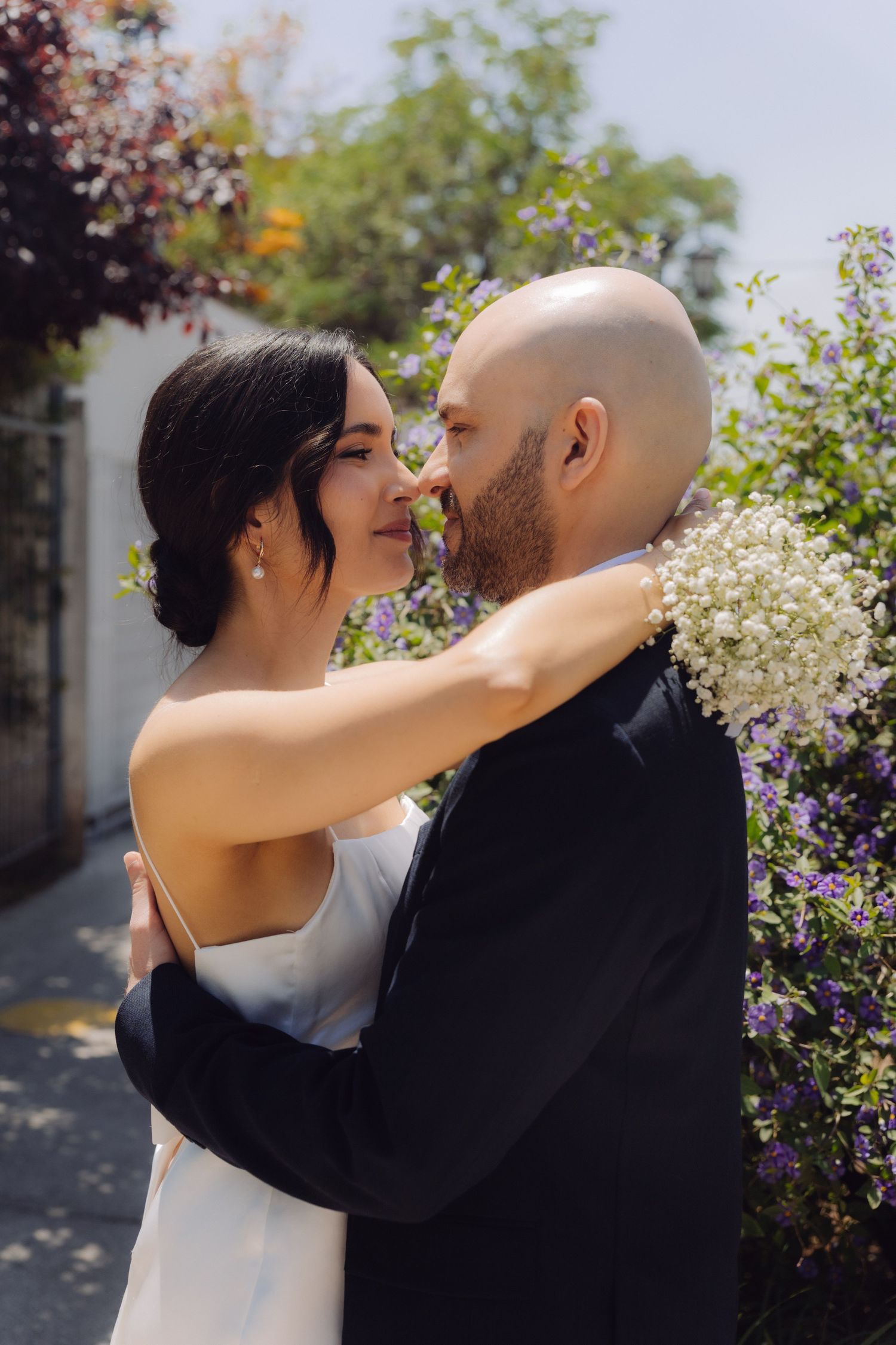 Bride and groom sharing a romantic moment surrounded by purple and white flowers outdoors.
