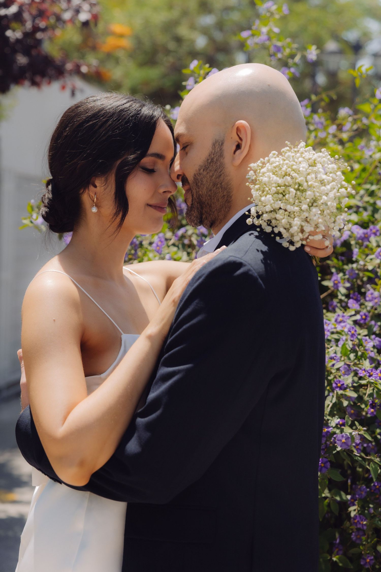 Wedding couple embracing closely with the groom holding white baby's breath flowers outdoors.