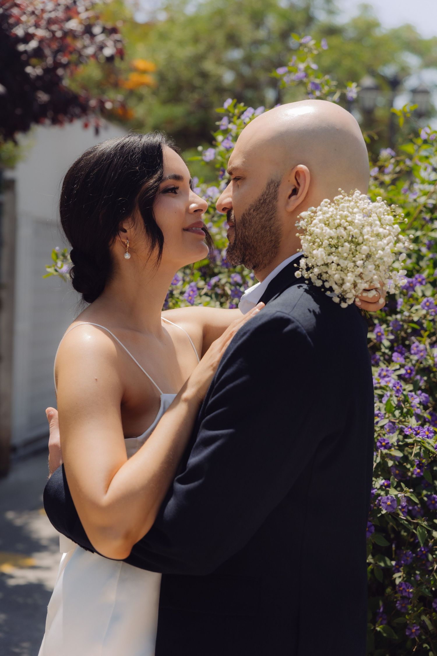 Newlyweds sharing an intimate nose-to-nose moment surrounded by blooming purple garden flowers.