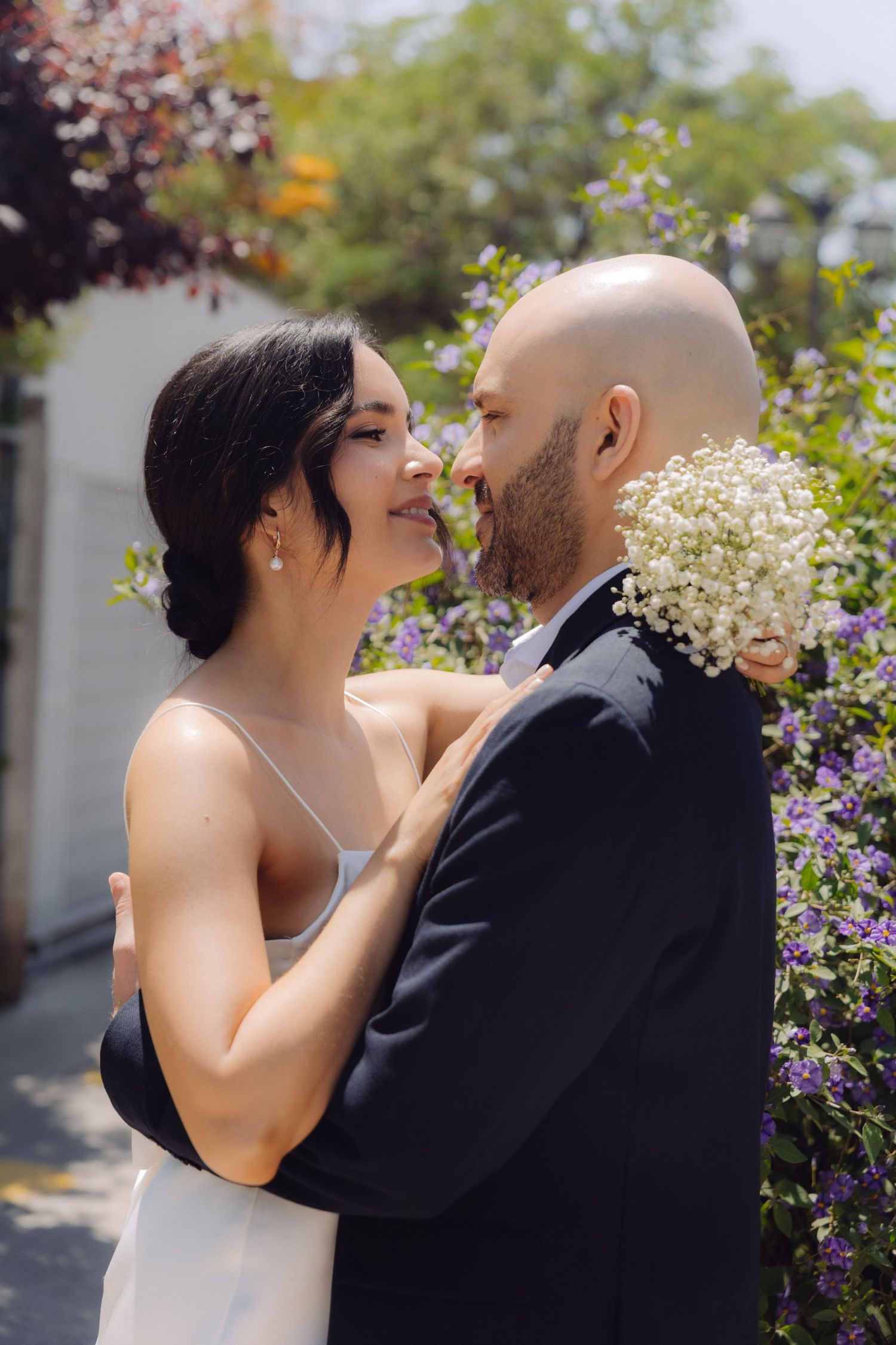Bride and groom in a tender embrace with white baby's breath bouquet in sunny garden.