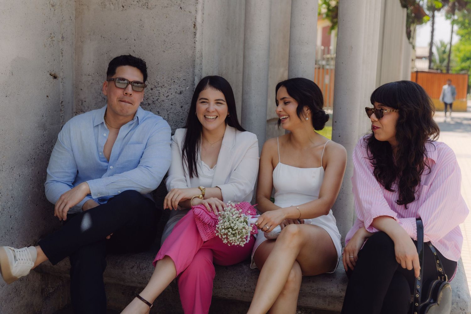 Group of four friends sitting on outdoor steps, smiling together at a casual gathering.