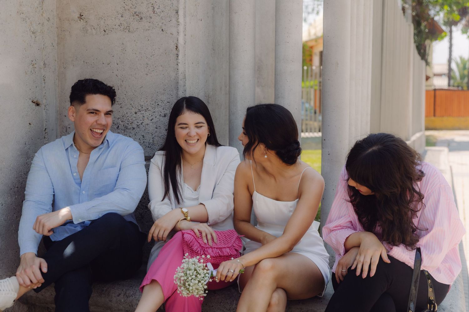 Four friends laughing and enjoying conversation while seated outdoors against concrete columns.