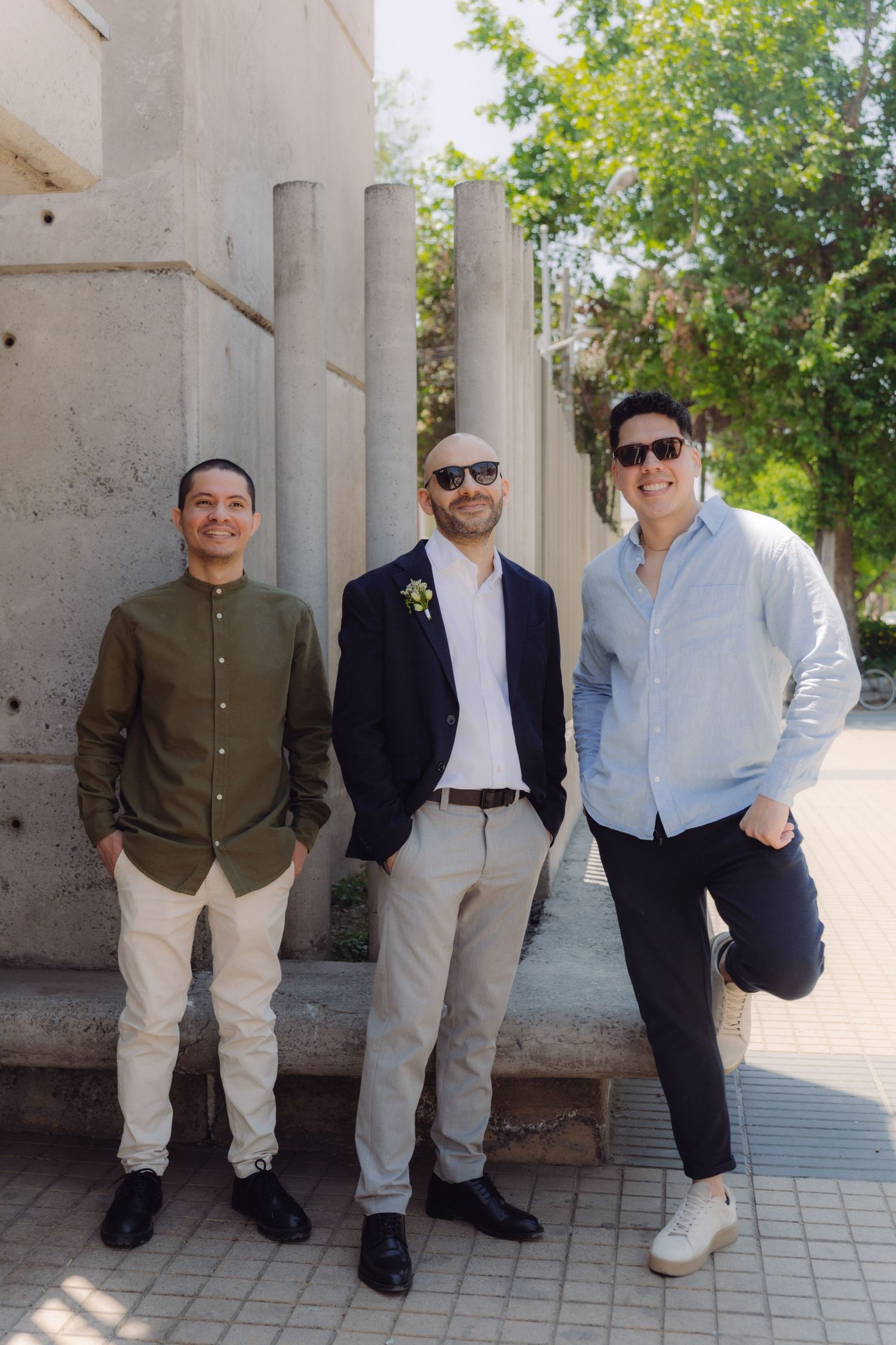 Three well-dressed men standing outdoors near concrete pillars, posing for a sunny day photo.