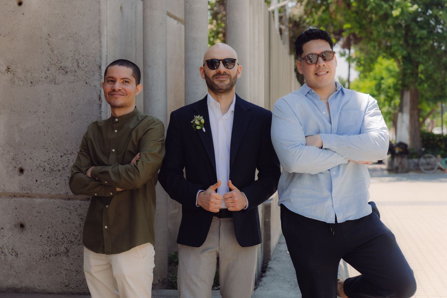 Three men standing with arms crossed near concrete columns, posing confidently outdoors.