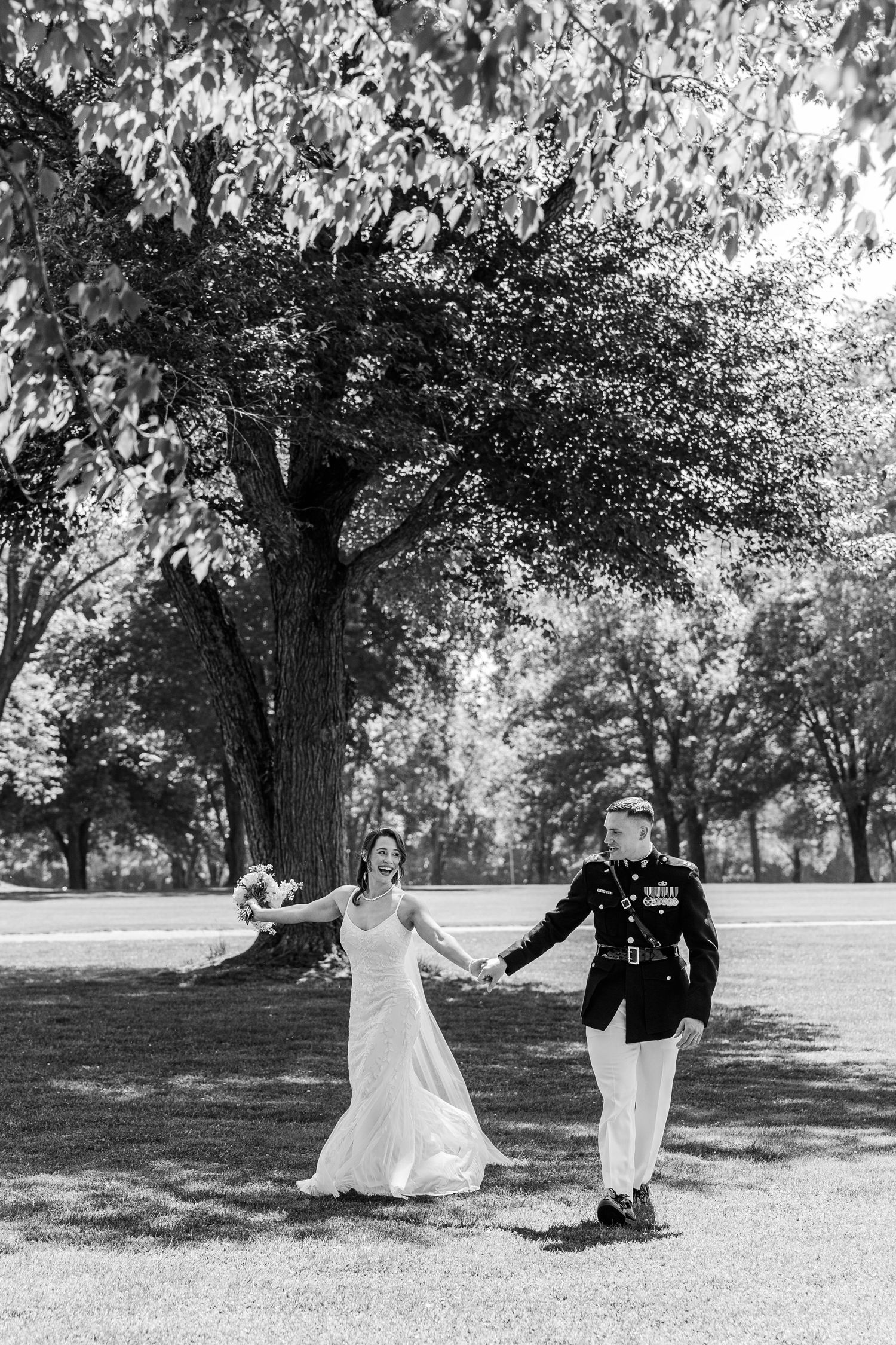 Black and white photo of a bride and Marine groom holding hands walking in a park on their wedding day.