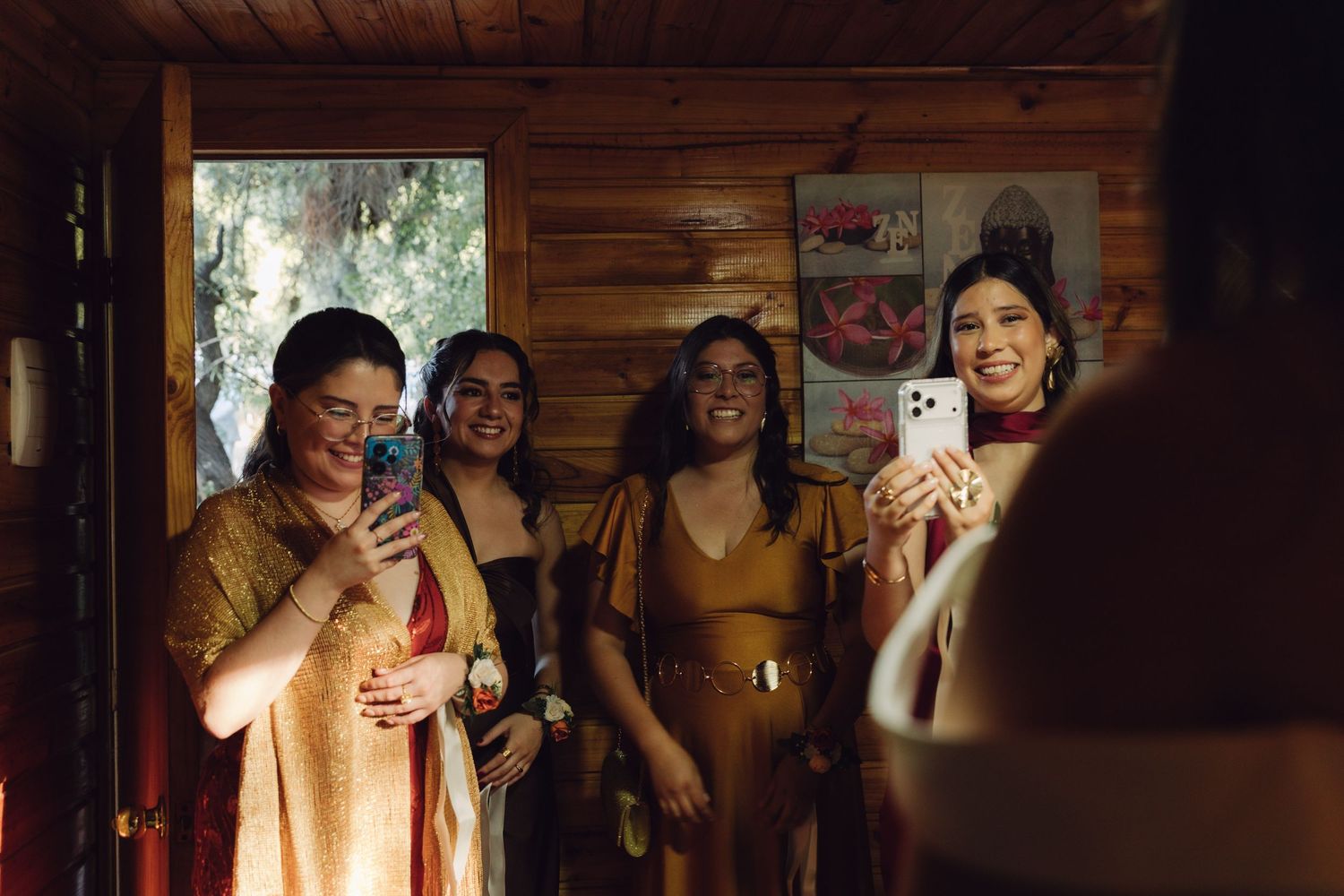 Group of women in formal attire smiling and taking photos inside a wooden cabin.