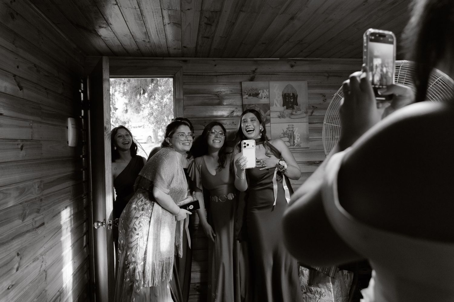 Black and white photo of women in formal dresses posing for photos in wooden cabin.