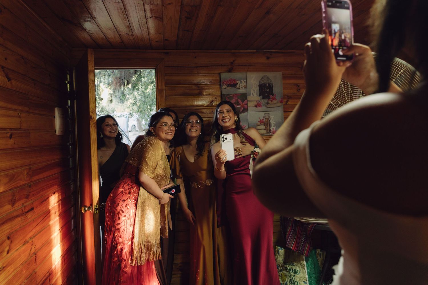 Women in formal gowns posing for photos inside warmly lit rustic wooden cabin interior.