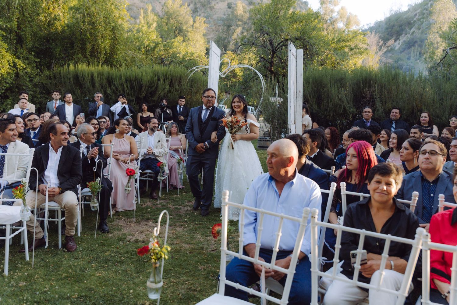 Bride and groom walk down the aisle as wedding guests watch at an outdoor garden ceremony.