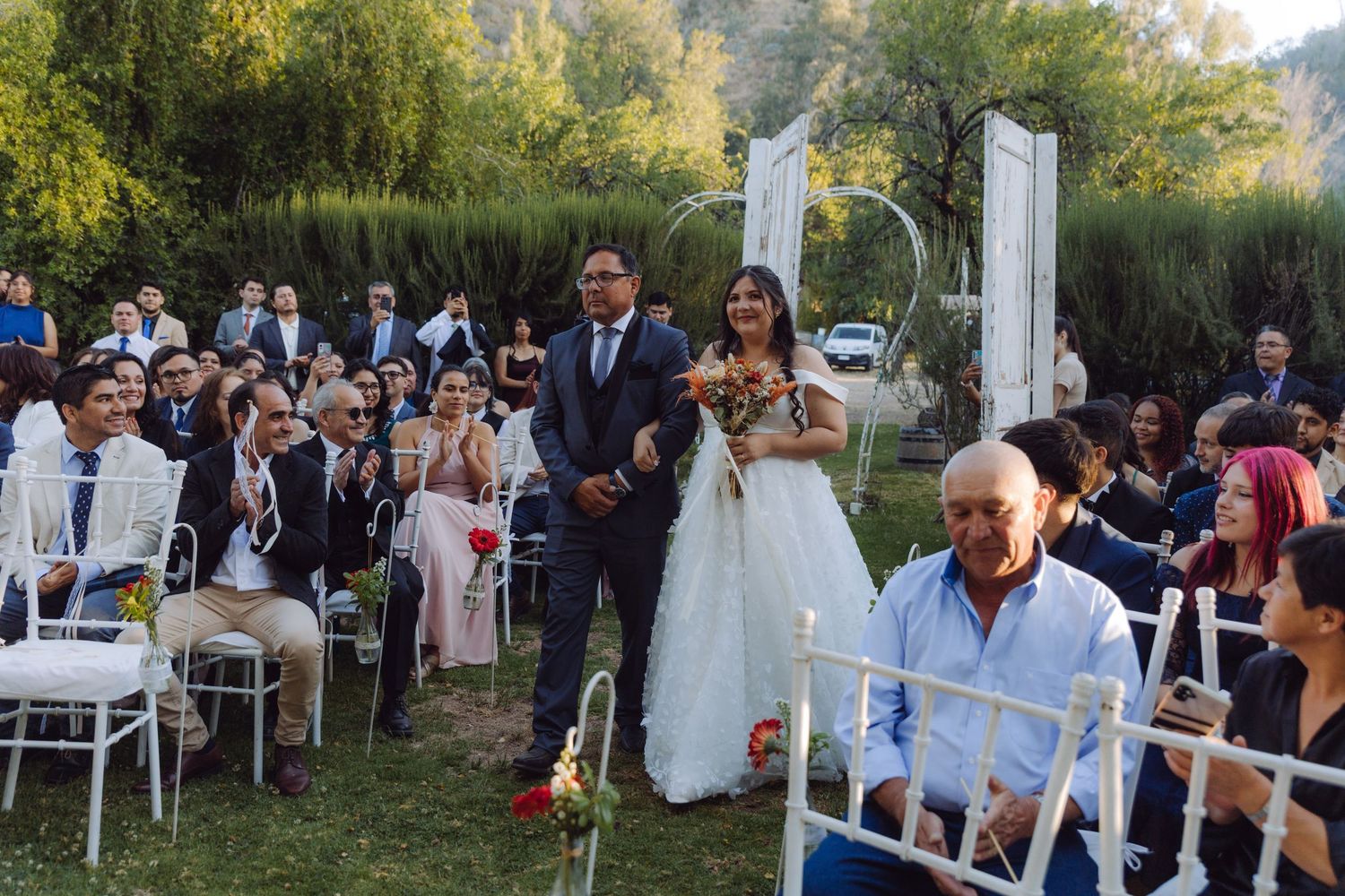 Bride and groom proceed down the aisle at an outdoor garden wedding ceremony with seated guests.