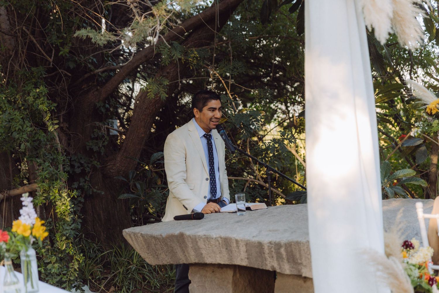 Wedding officiant stands at stone altar podium during an elegant outdoor garden ceremony.