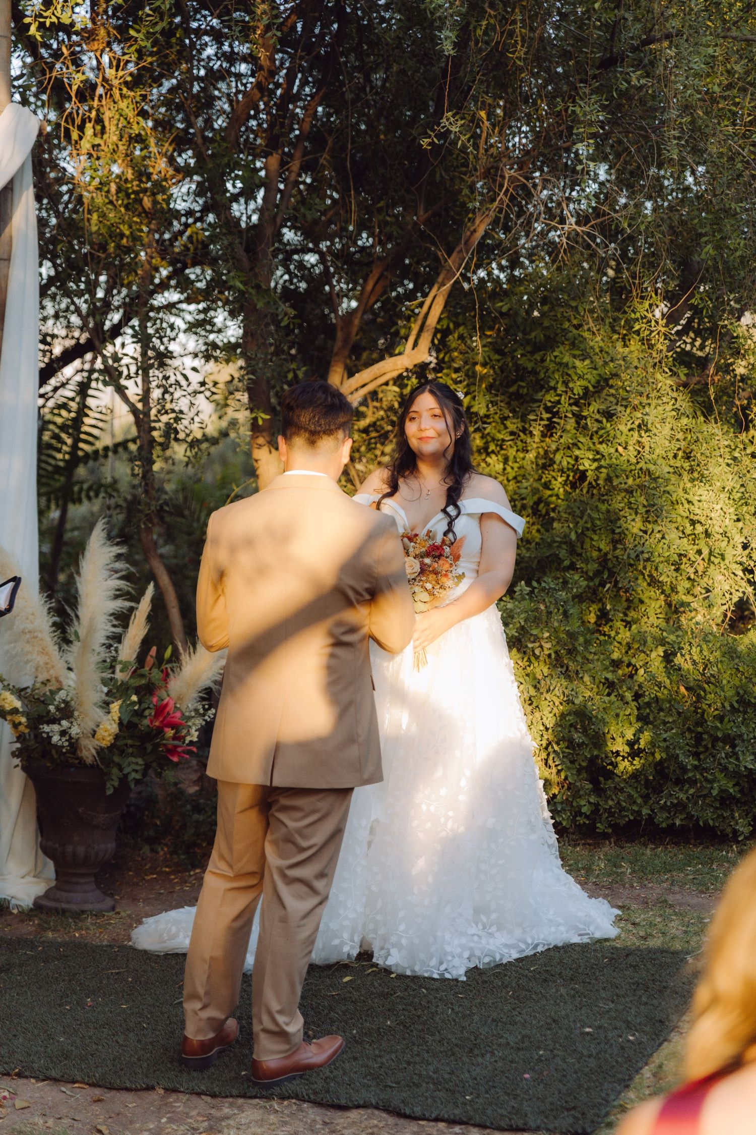 Bride smiles at groom during intimate outdoor garden wedding ceremony surrounded by lush greenery.
