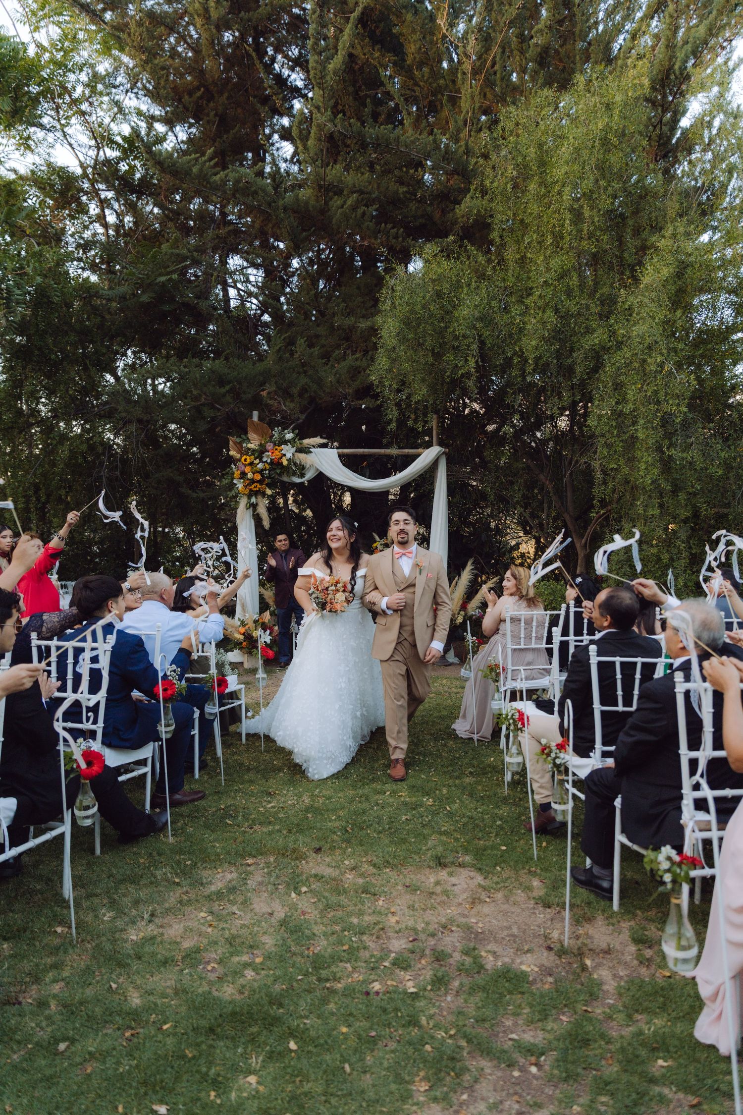 Joyful newlyweds walk down aisle as guests celebrate at elegant outdoor garden wedding ceremony.
