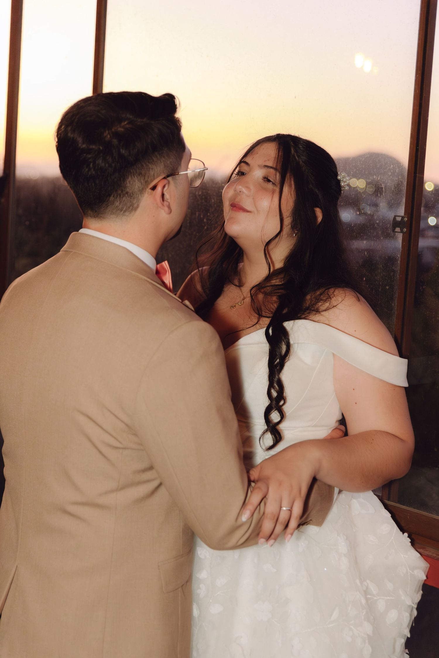 Bride gazes lovingly at groom during romantic sunset moment at indoor wedding venue.