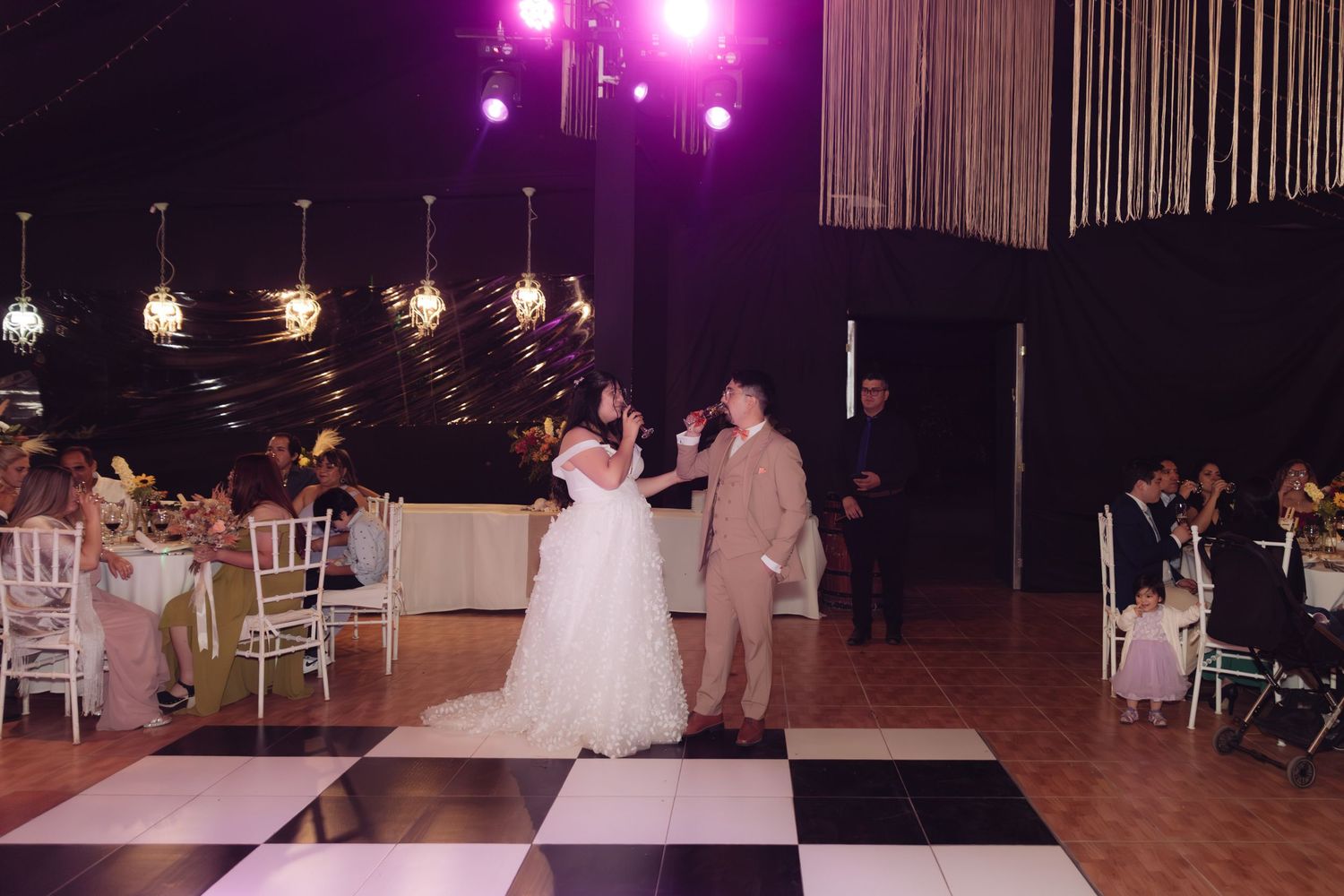 Bride and groom share first dance on black and white checkered dance floor in elegant wedding reception hall.