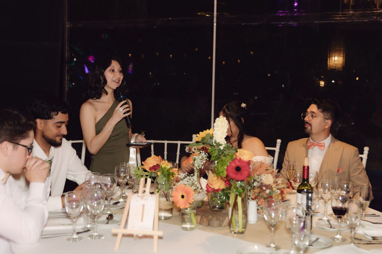 Woman giving a toast speech at an elegant wedding reception dinner table with floral centerpieces.
