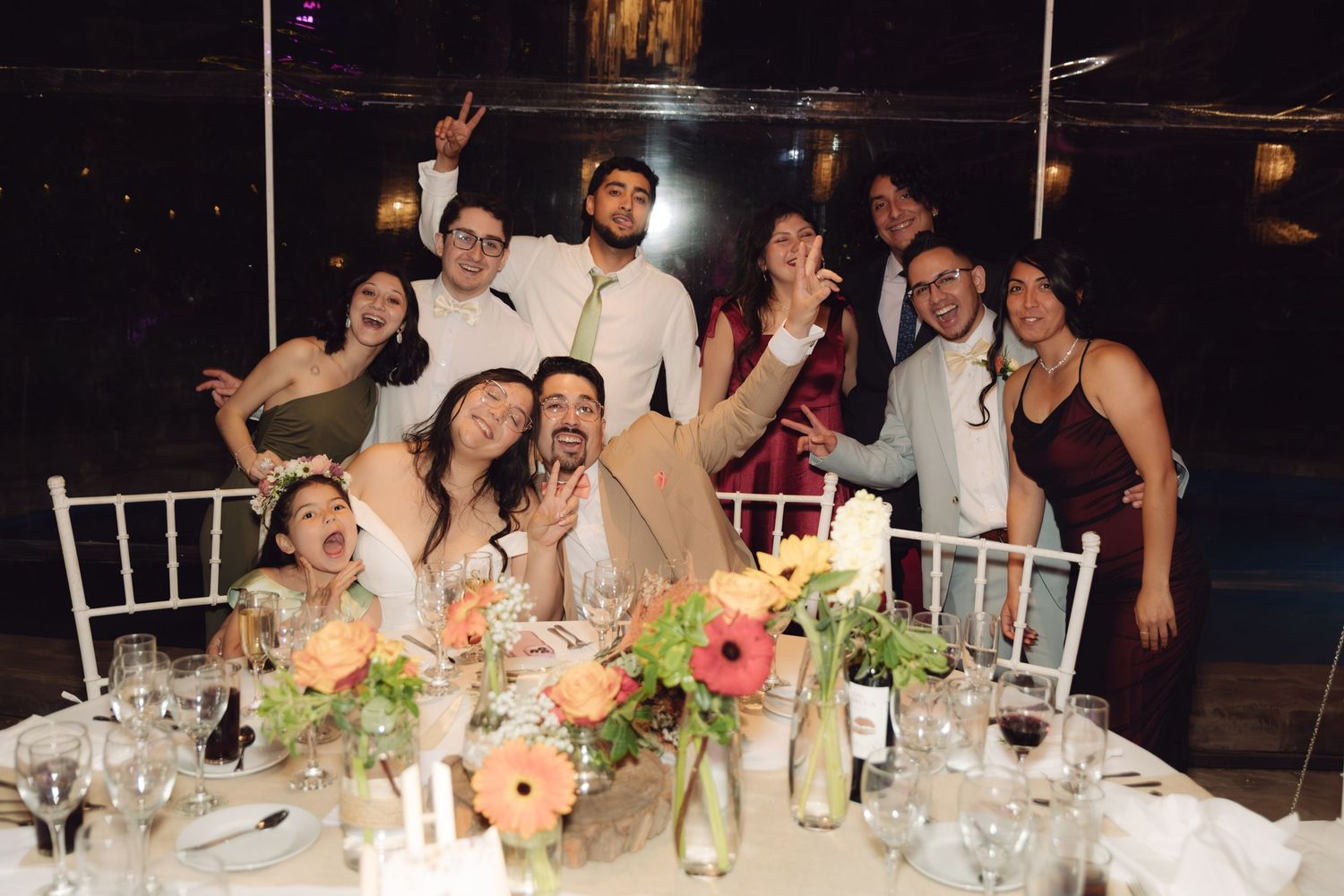 Smiling wedding party guests posing together at a beautifully decorated reception dinner table.