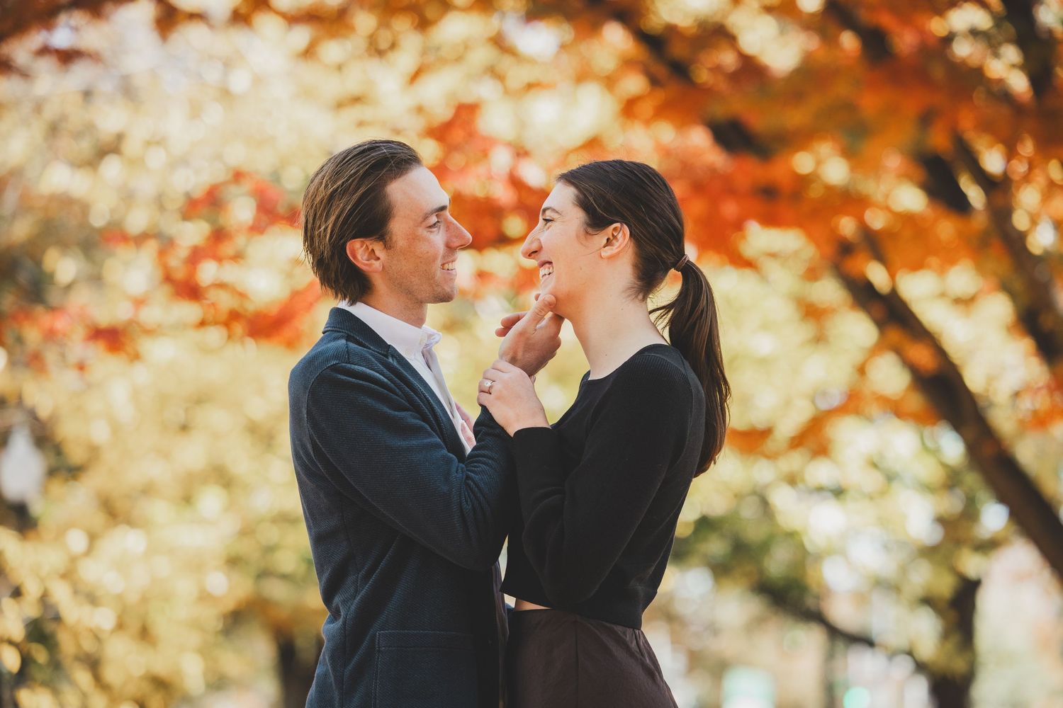 Couple sharing a romantic moment outdoors surrounded by vibrant autumn foliage in warm red and orange tones at Lincoln Memorial Park in DC