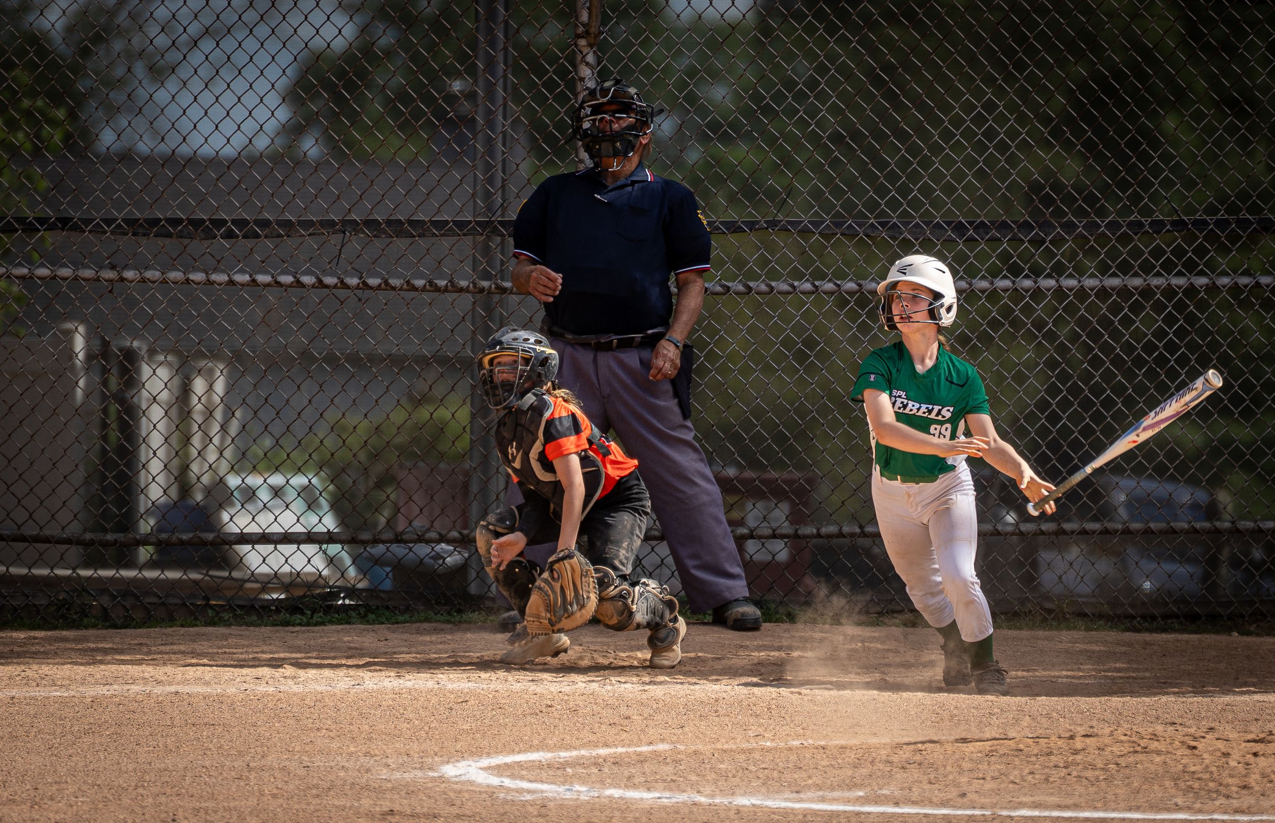 Youth softball player watches her hit soar into the outfield.