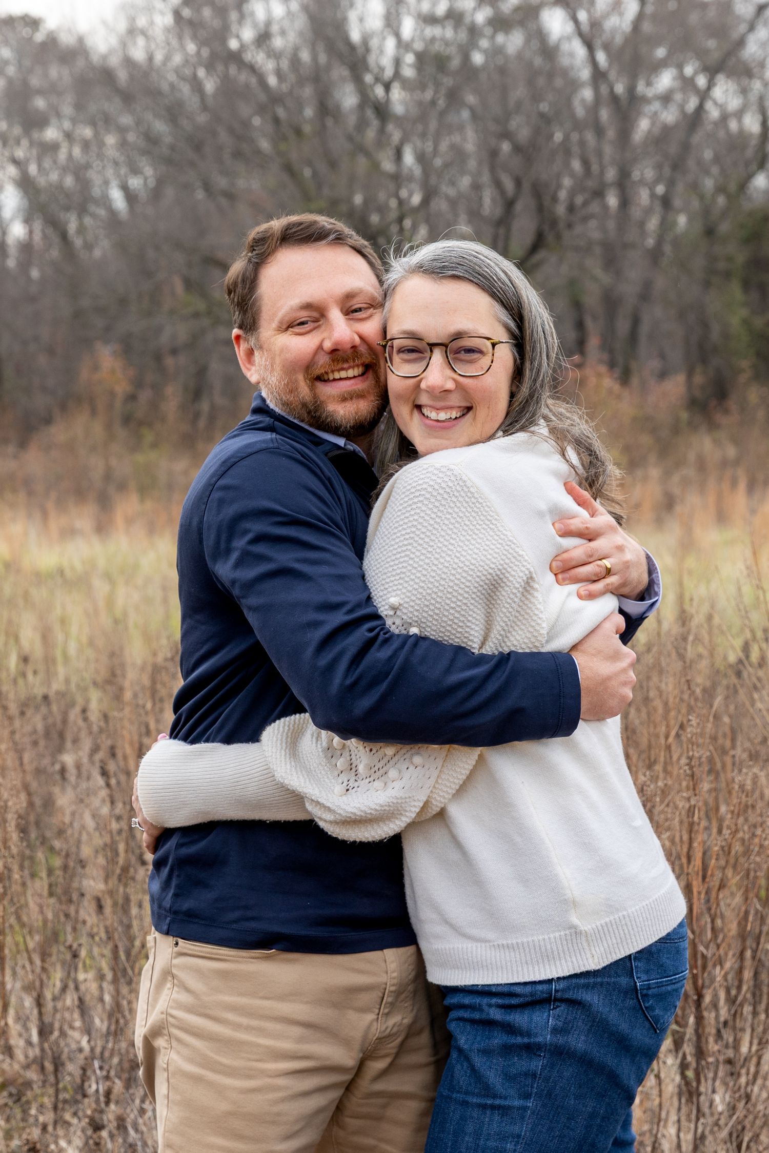 Couple sharing warm embrace in field during fall photo session.