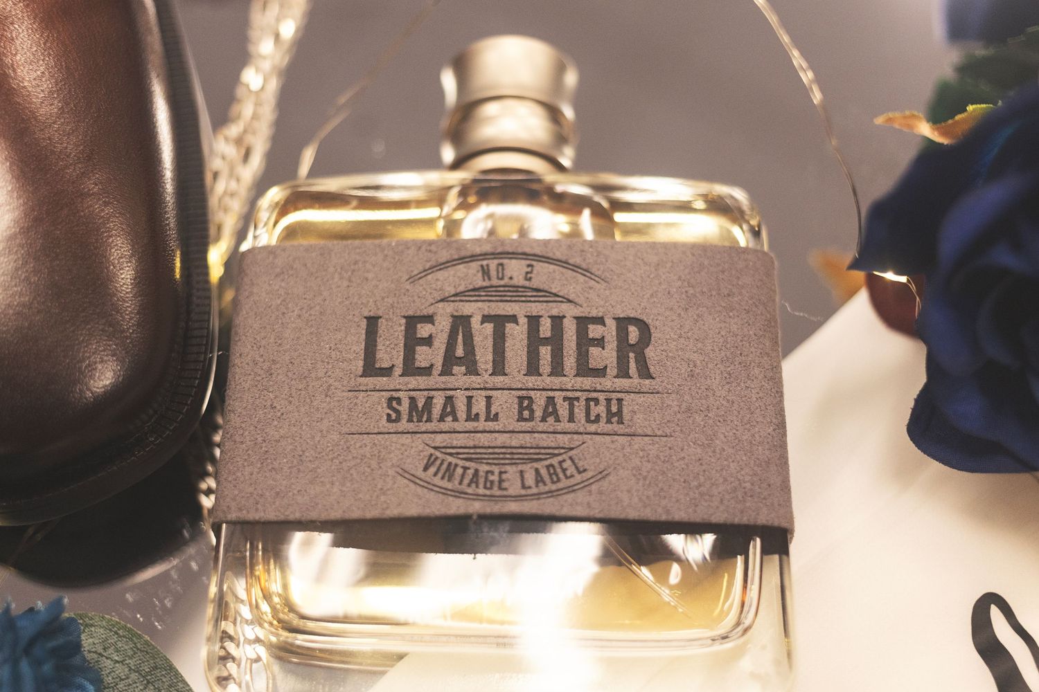 Close-up of a leather small batch vintage label on a glass perfume bottle with blue flowers in background.