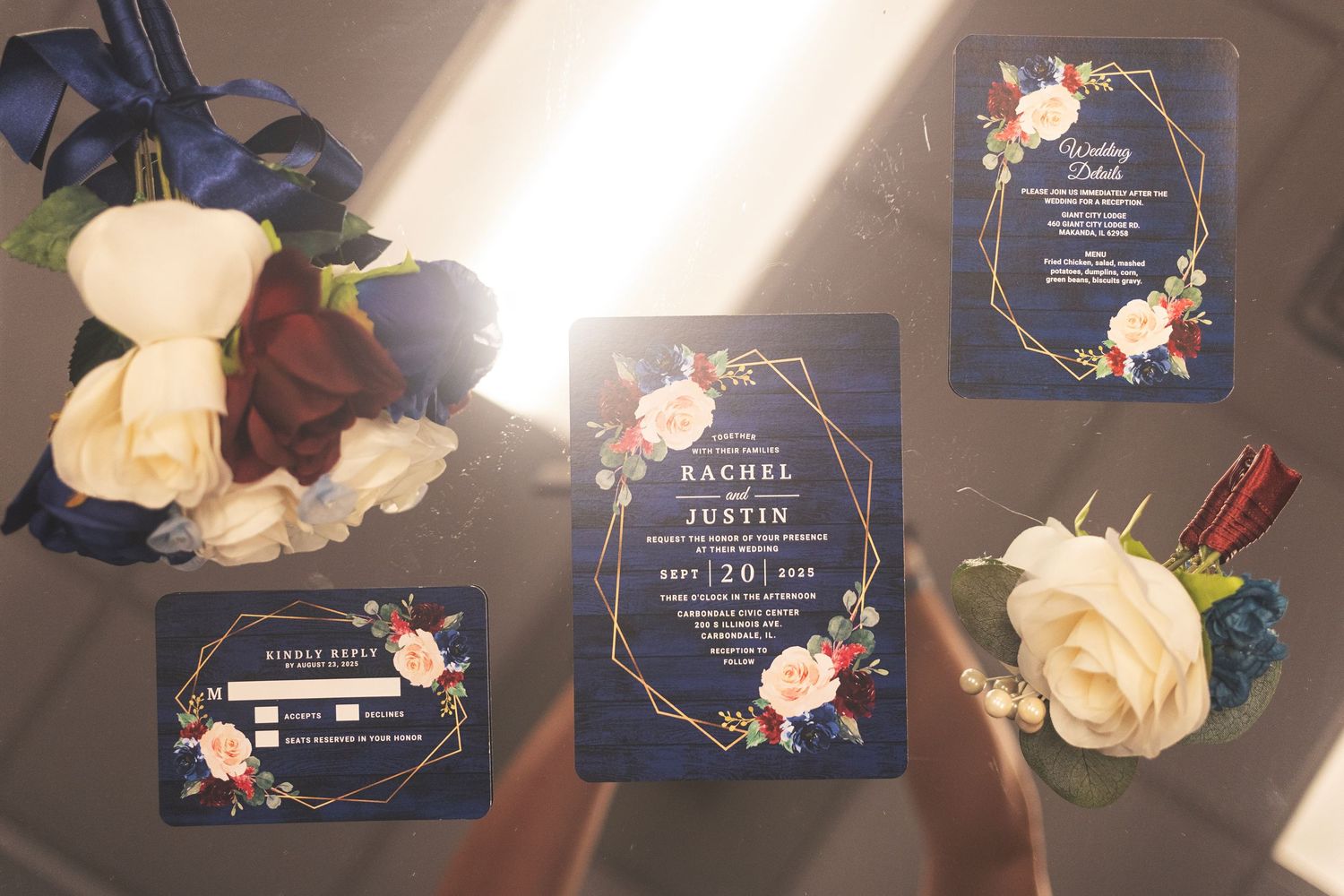Navy blue wedding invitation suite with gold geometric frames, floral accents, and matching stationery displayed with roses.