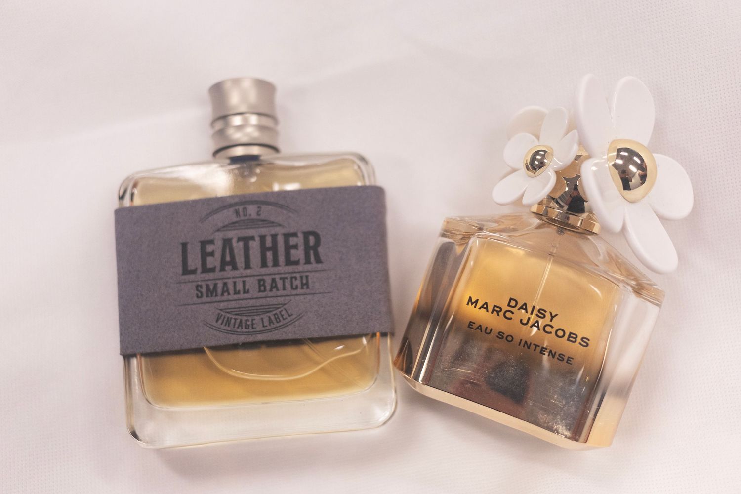 Two perfume bottles side by side: Leather Small Batch cologne and Daisy Marc Jacobs Eau So Intense fragrance.