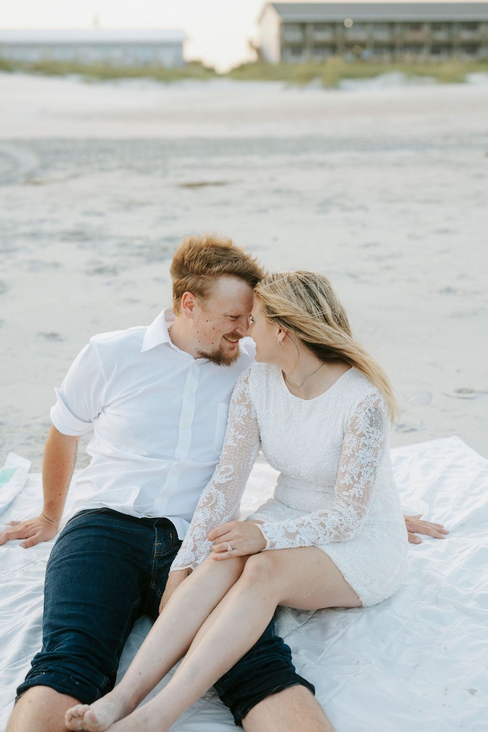 Romantic couple sitting close together on a blanket on the beach, gazing into each other's eyes.