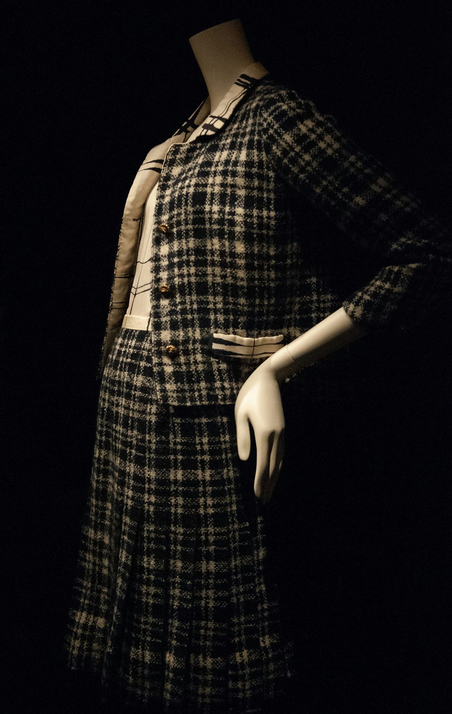 Vintage plaid tweed skirt suit on mannequin, featuring gold buttons and cream trim, displayed against dark background.