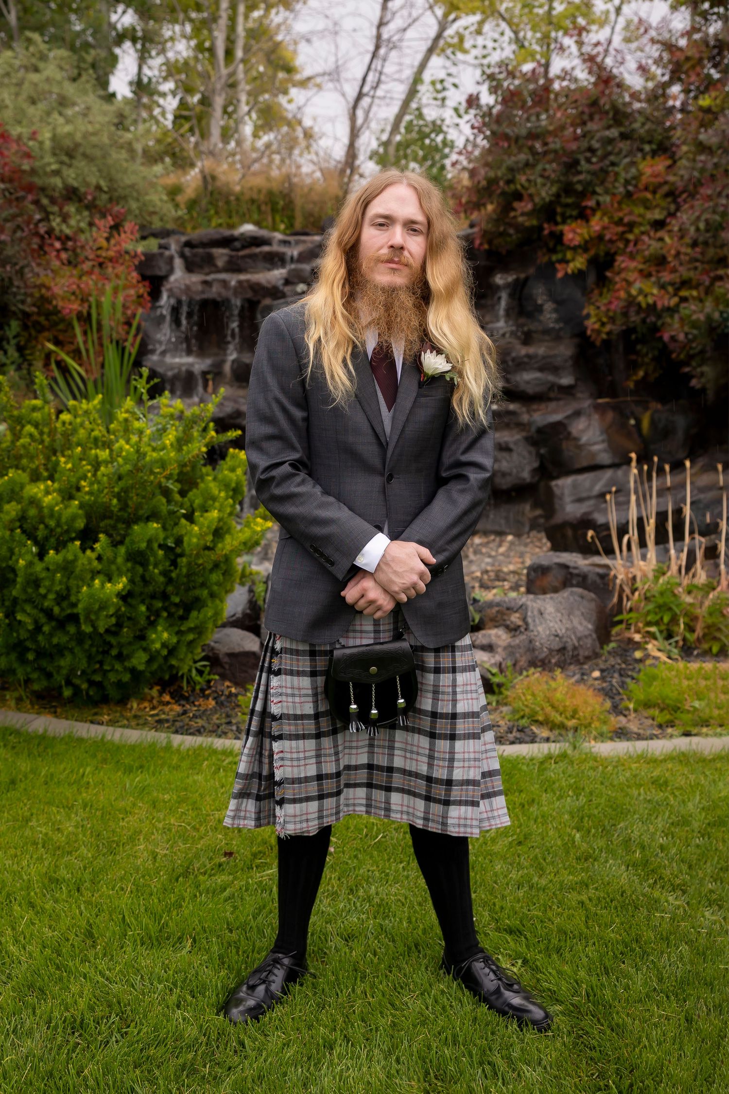 groom wear gray and a kilt posing in front of water feature Castle Gardens Kuna Idaho ©Milestones Studios LLC