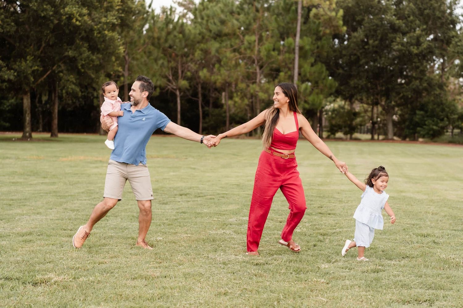 A family of three posing together outdoors in a park setting during golden hour.