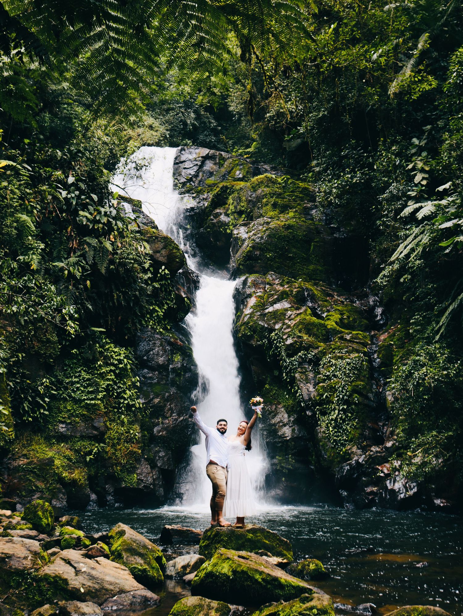 Person standing before a lush tropical waterfall surrounded by green jungle foliage.