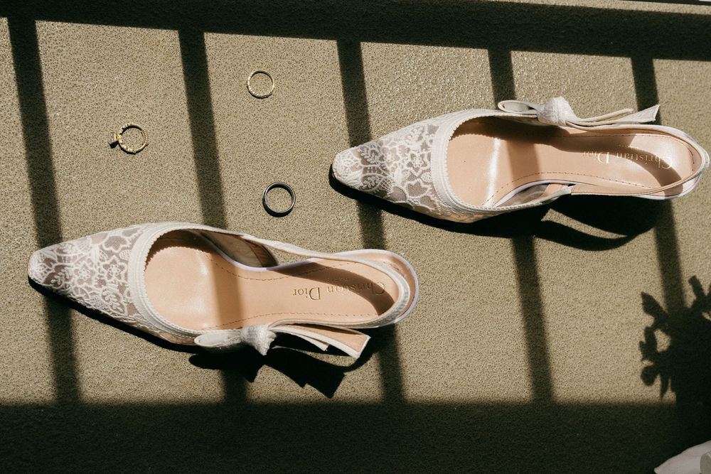Elegant white lace slingback wedding heels with gold rings on a sunlit surface.