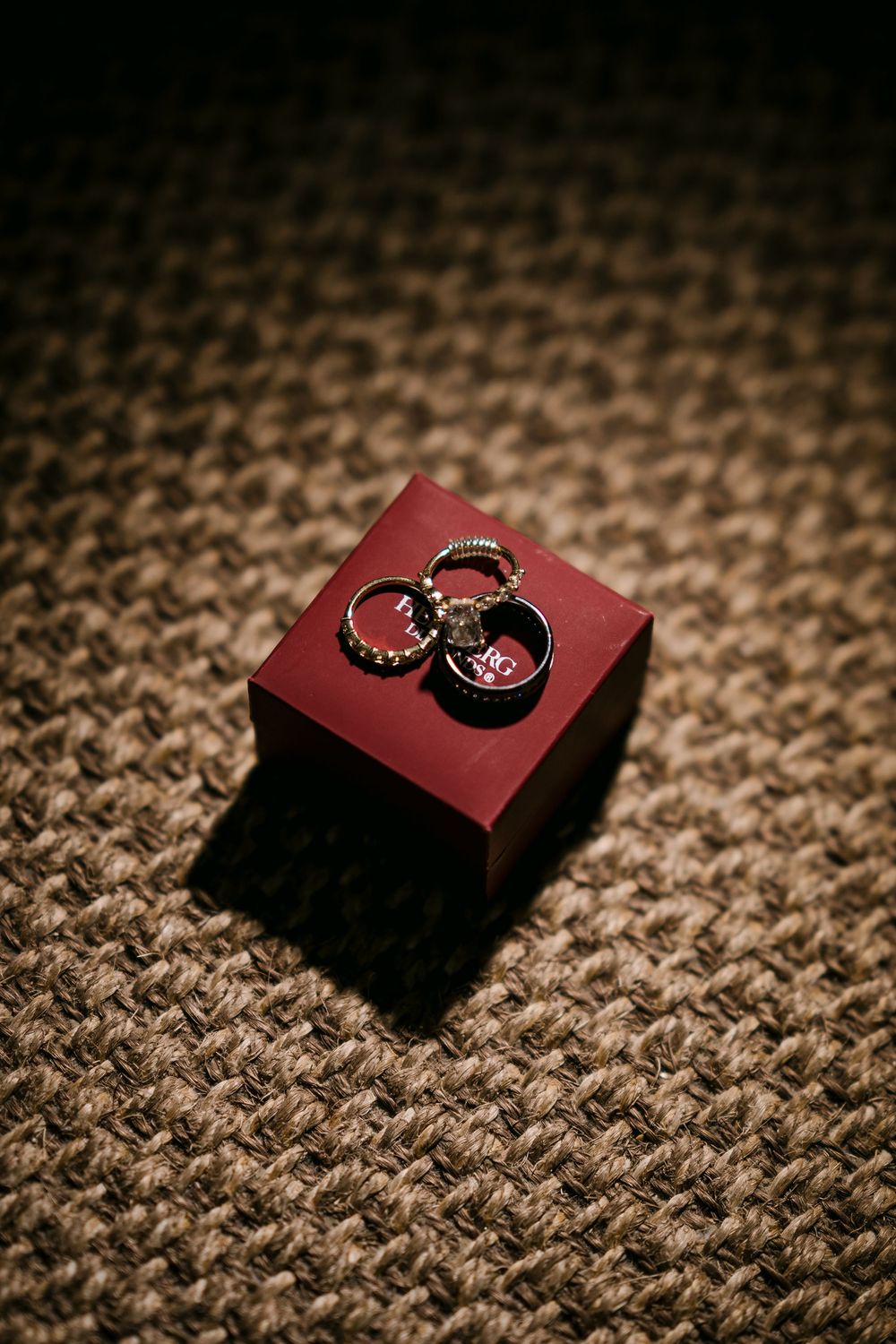 Three gold rings displayed on a small red jewelry box on a woven brown surface.