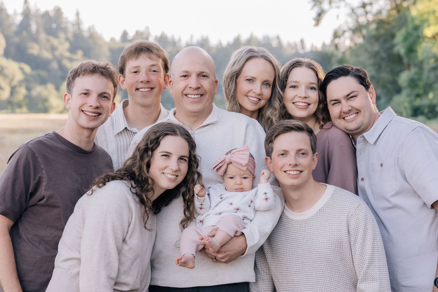 Large family group portrait with parents, adult children, and baby outdoors in a lush green field setting.