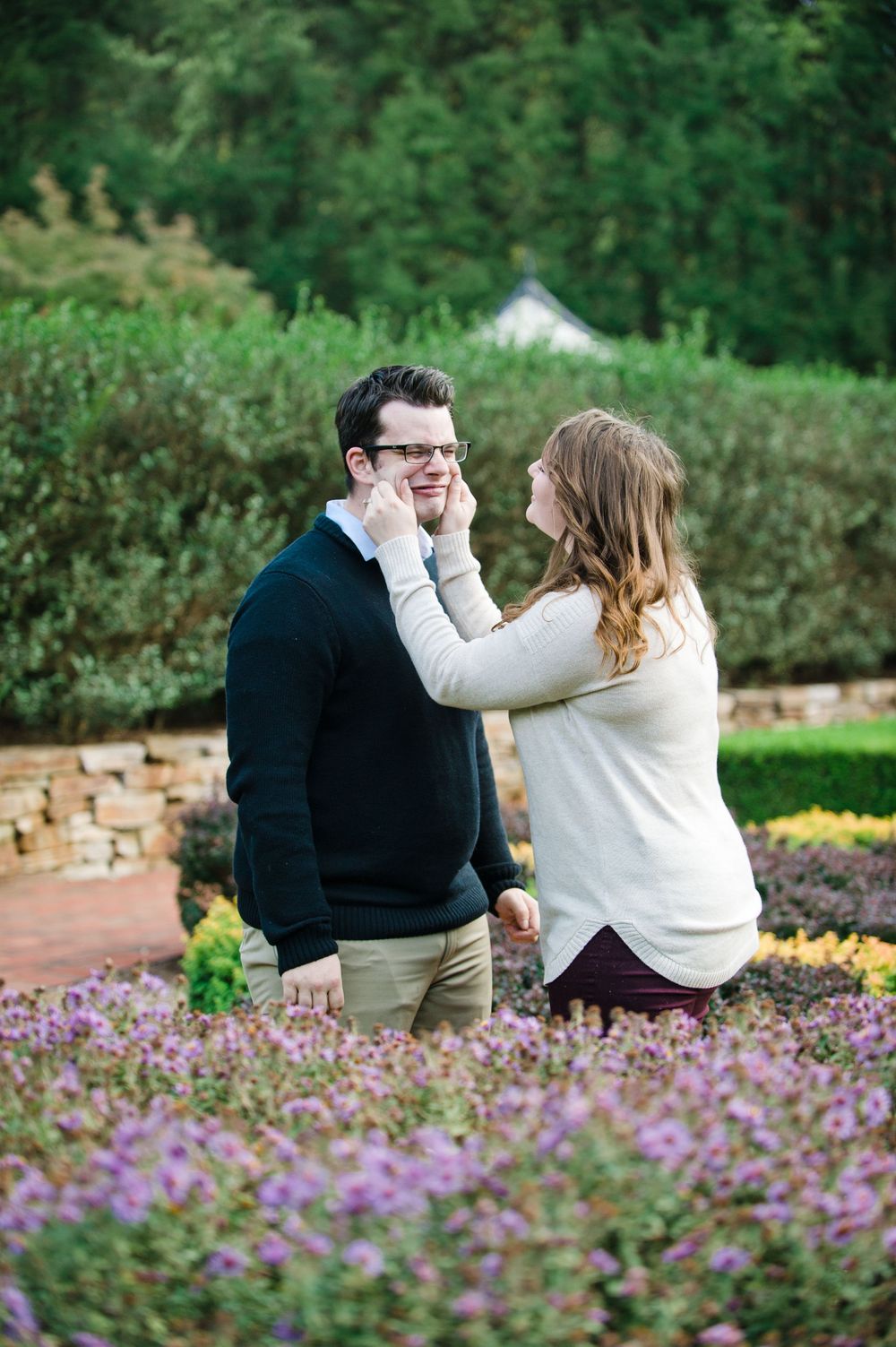 Playful woman adjusting mans glasses while standing in a vibrant flower garden together.