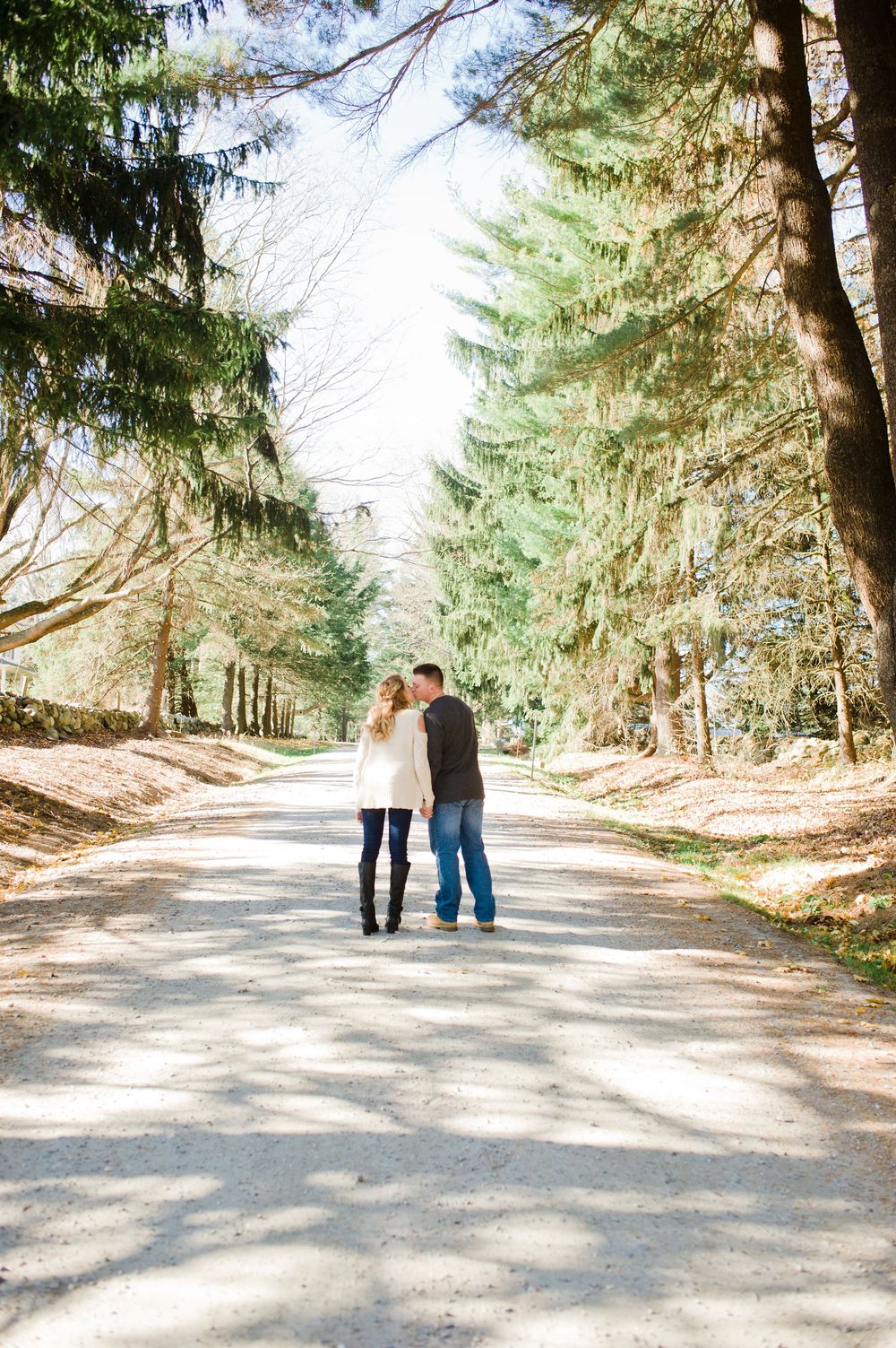 Couple sharing a tender kiss while standing together on a tree-lined path during engagement session.