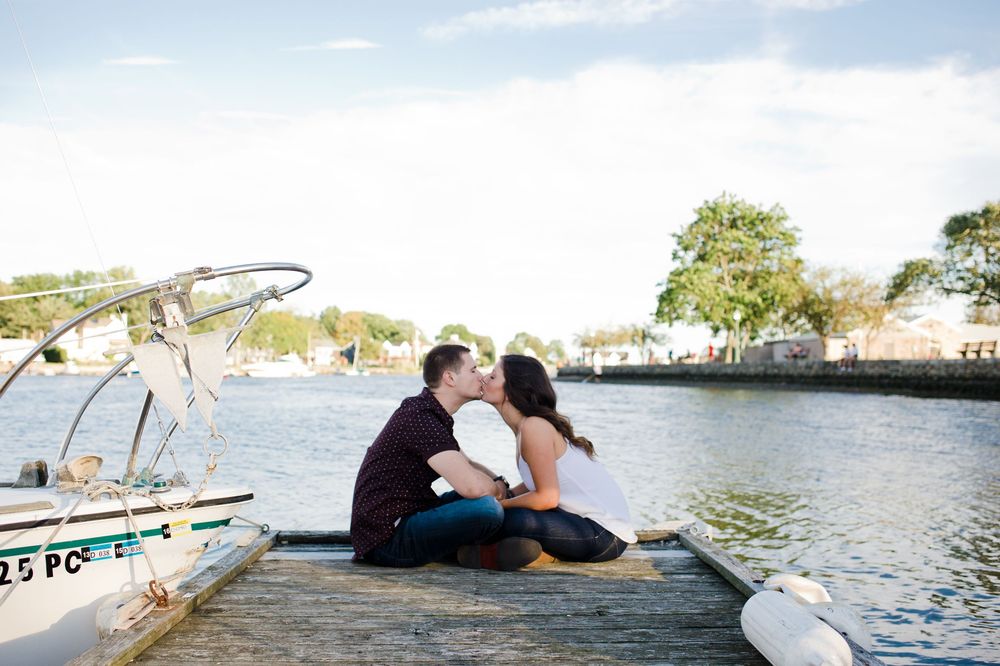 Couple sharing a romantic kiss on a wooden dock beside a boat on a calm waterway.