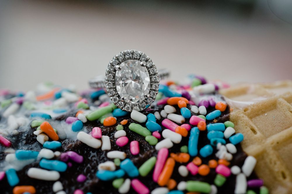 A stunning oval diamond halo engagement ring displayed on colorful sprinkles.