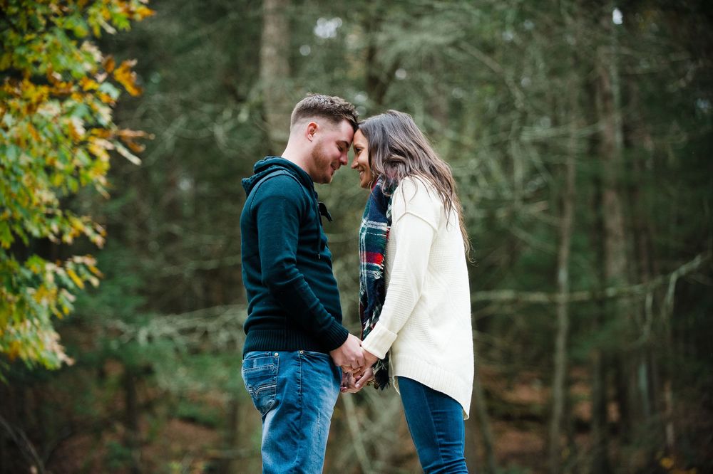 Young couple holding hands and touching foreheads romantically in an autumn forest setting.
