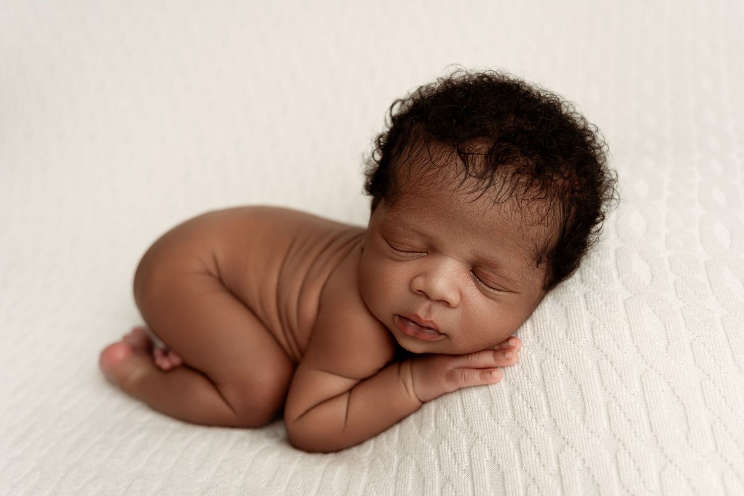 Peaceful newborn baby sleeping curled up on white textured blanket in classic posed newborn photography session.